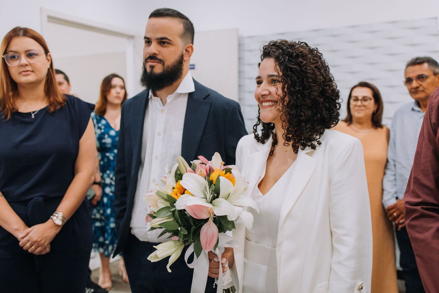 Wedding guests gather and mingle during a celebration in a bright indoor venue with white walls.