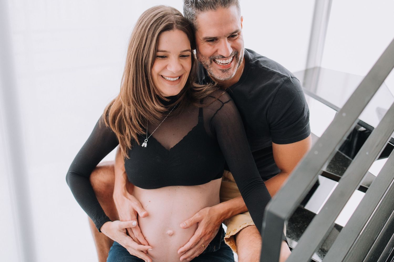 Couple shares intimate moment on staircase during maternity photoshoot.