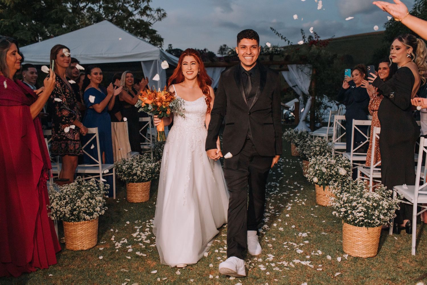 Newlyweds celebrate with guests throwing confetti at an outdoor evening wedding reception.