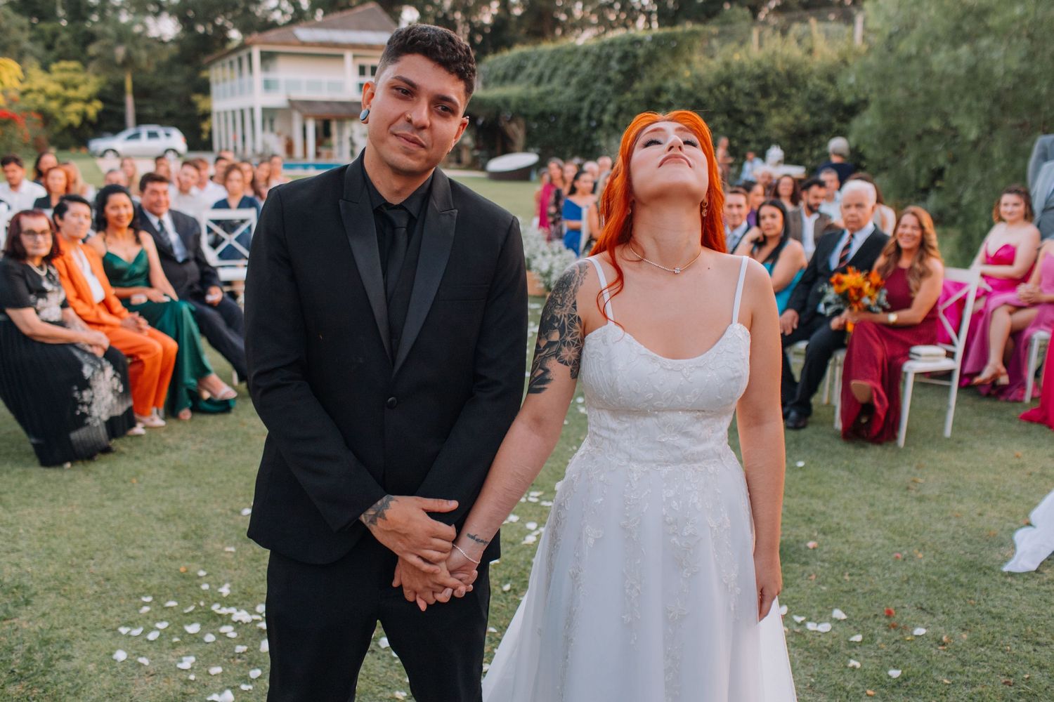 A joyful wedding celebration takes place outdoors with guests seated on the lawn during a sunny afternoon ceremony.