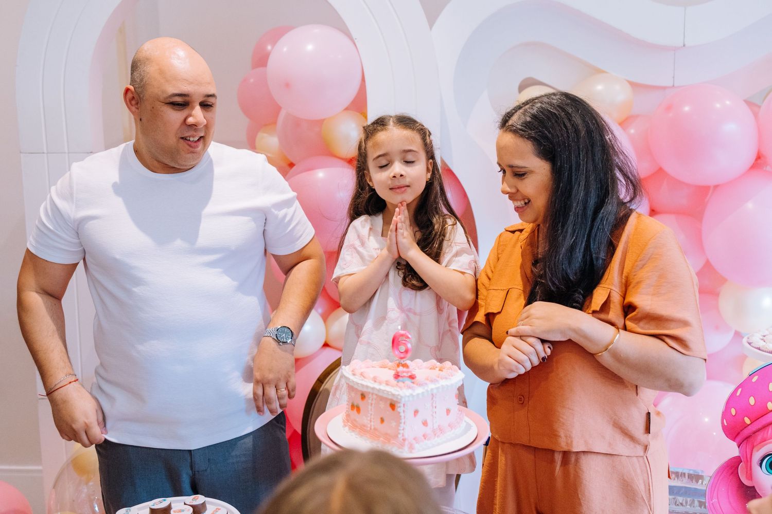 Pink balloon backdrop decorates a family photography session with casual attire and warm tones.