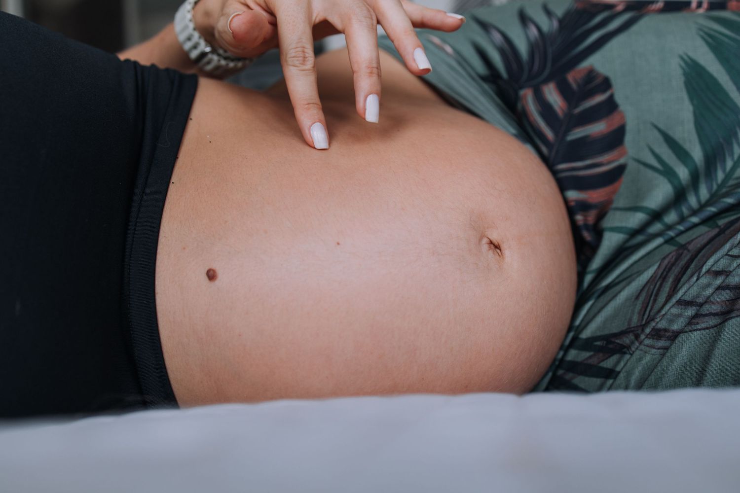 Close-up view of a pregnant belly against dark patterned fabric.