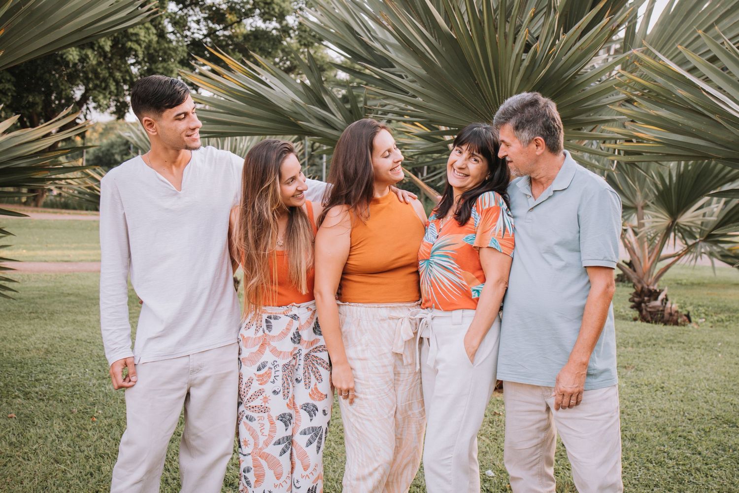 Coordinated family group photo with members wearing white and orange outfits under palm trees.