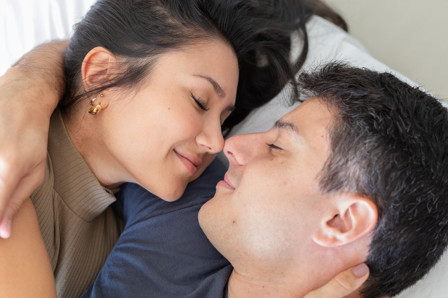 Romantic couple lying close together on a bed, sharing an intimate moment with eyes closed.