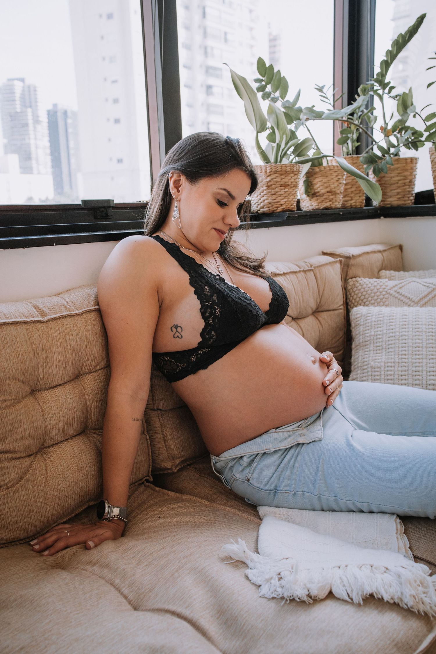 A maternity photo of someone reclining on a beige couch near windows.