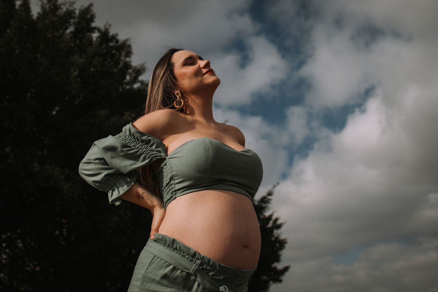 Dramatic sky backdrop for outdoor maternity portraits in sage green dress.