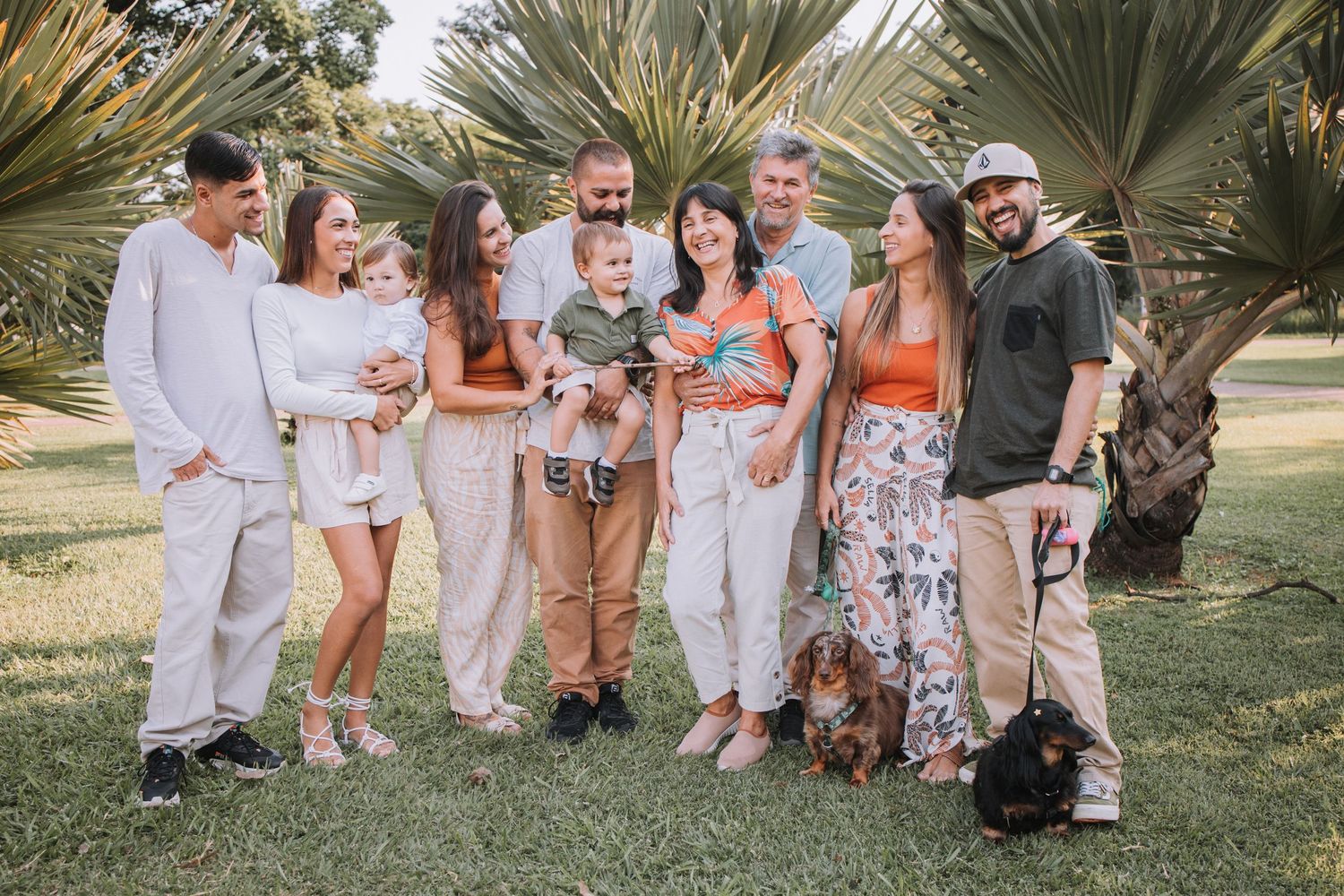 Extended family wearing coordinated orange and white outfits poses for photo under palm trees.