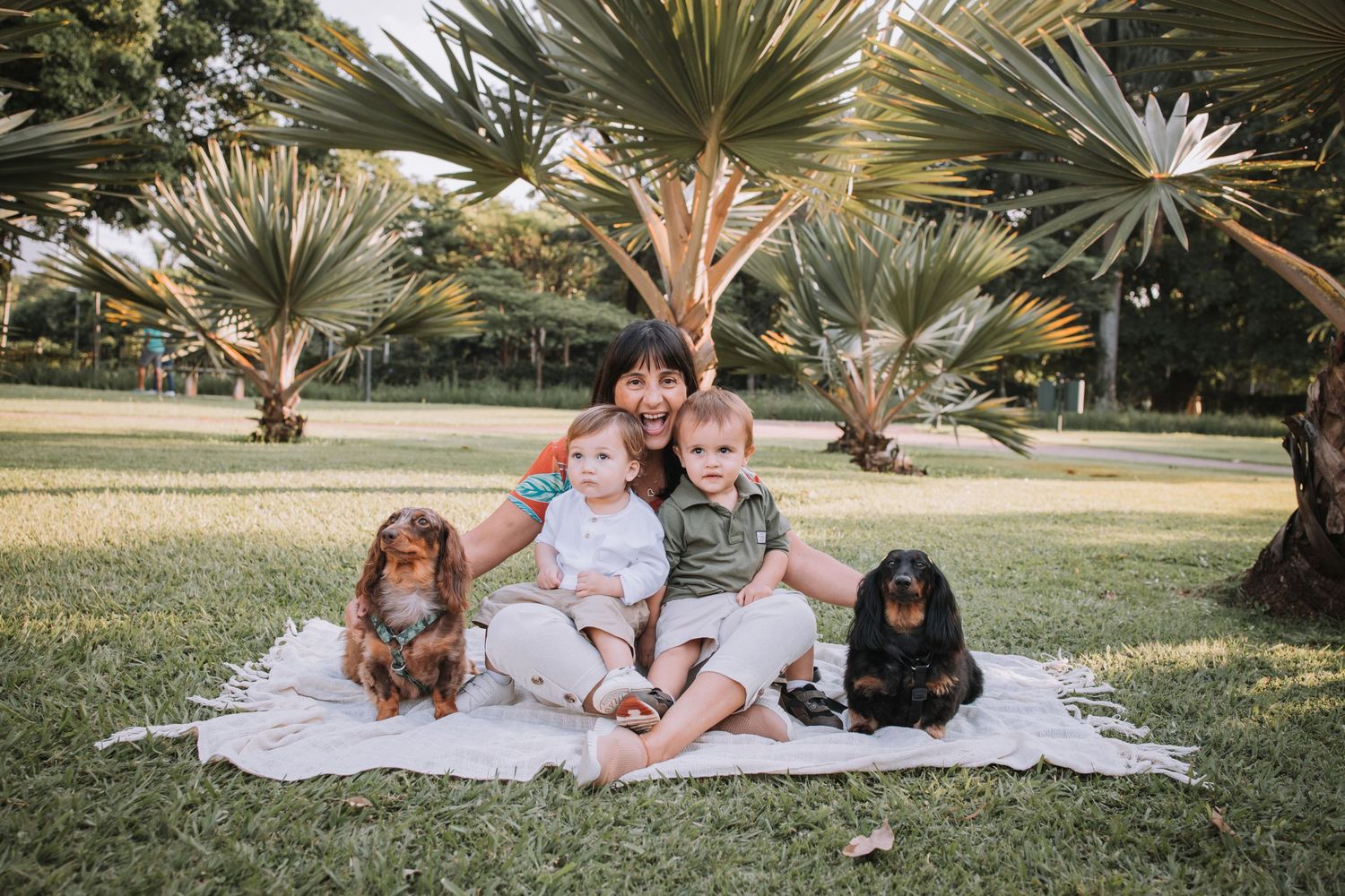 Group relaxing on white blanket under palm trees during outdoor photoshoot.