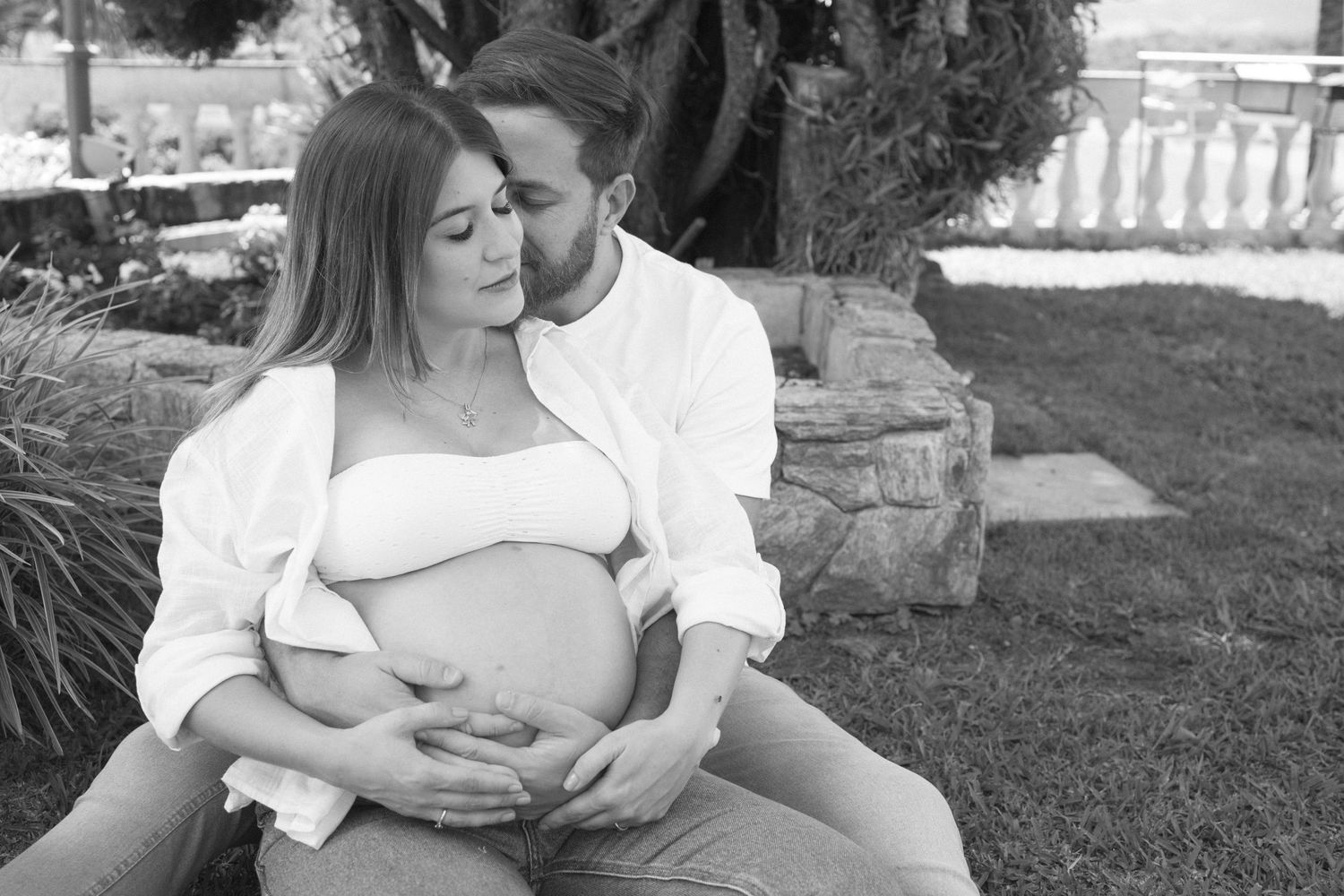 A tender maternity photo in black and white showing an intimate embrace on a grassy lawn.