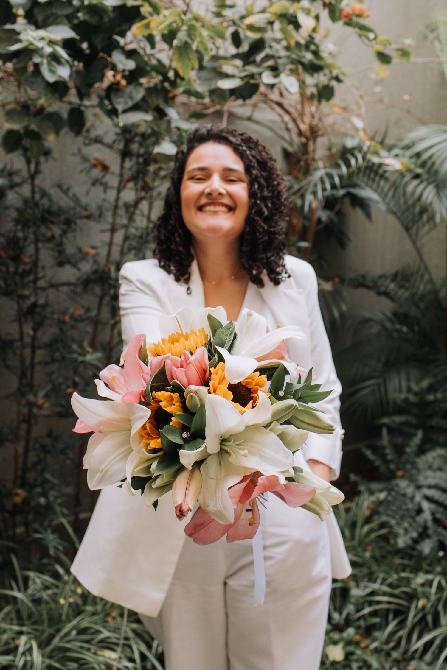 Someone in a crisp white suit holds a vibrant bouquet of pink and orange lilies against a lush garden backdrop.