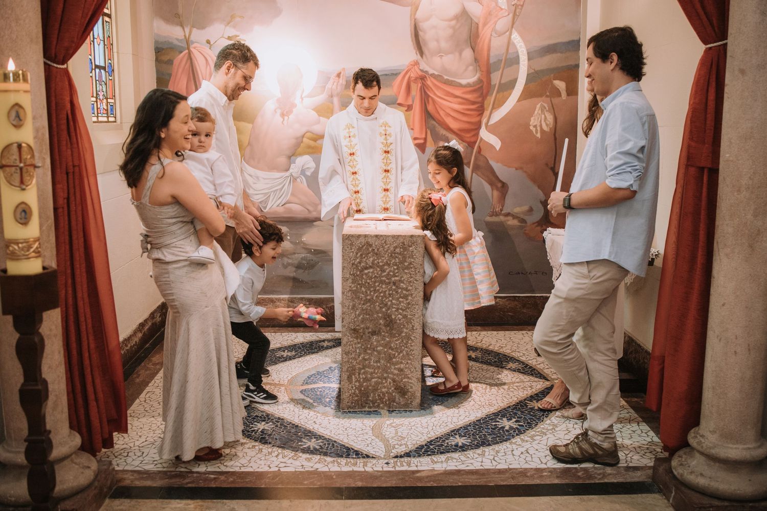 A baptism ceremony is conducted around a stone font in an ornate church setting.