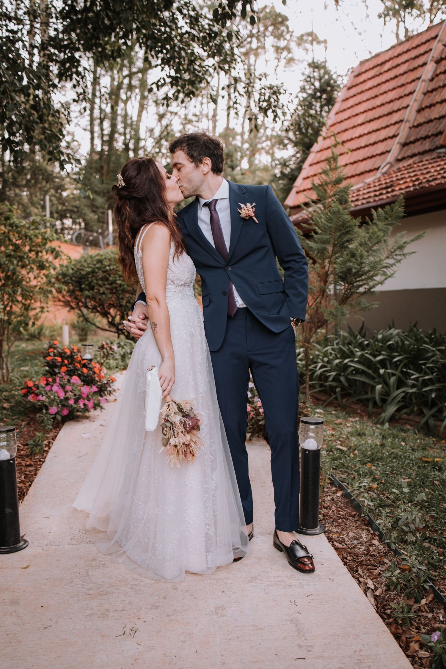 A romantic outdoor wedding scene with a couple in formal attire sharing a tender moment by a rustic building.