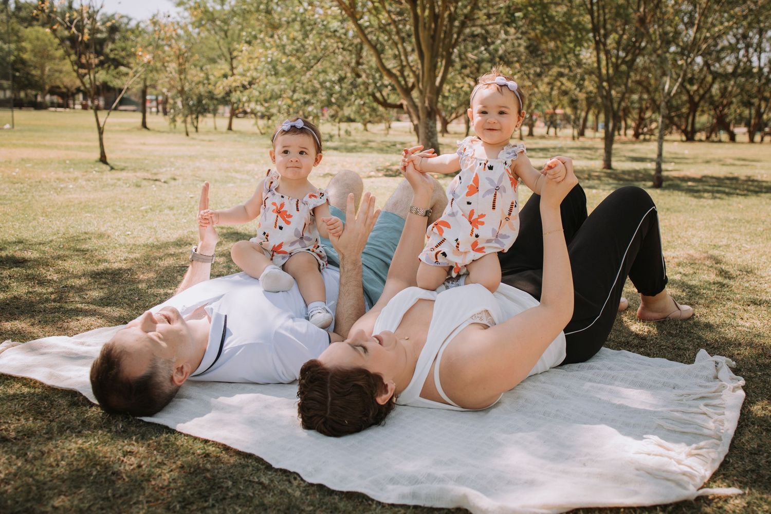 A relaxed family moment captured on a white blanket under shady trees.