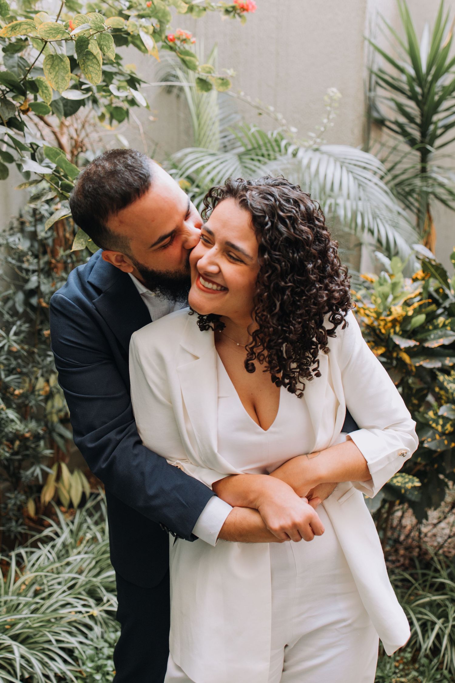 Couple embracing and laughing in a lush garden setting with tropical plants.