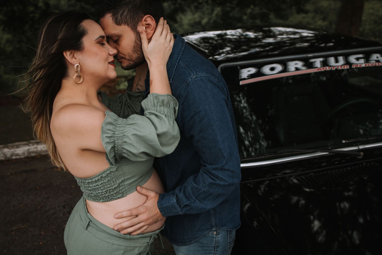 Romantic couple poses by vintage car during outdoor maternity session.