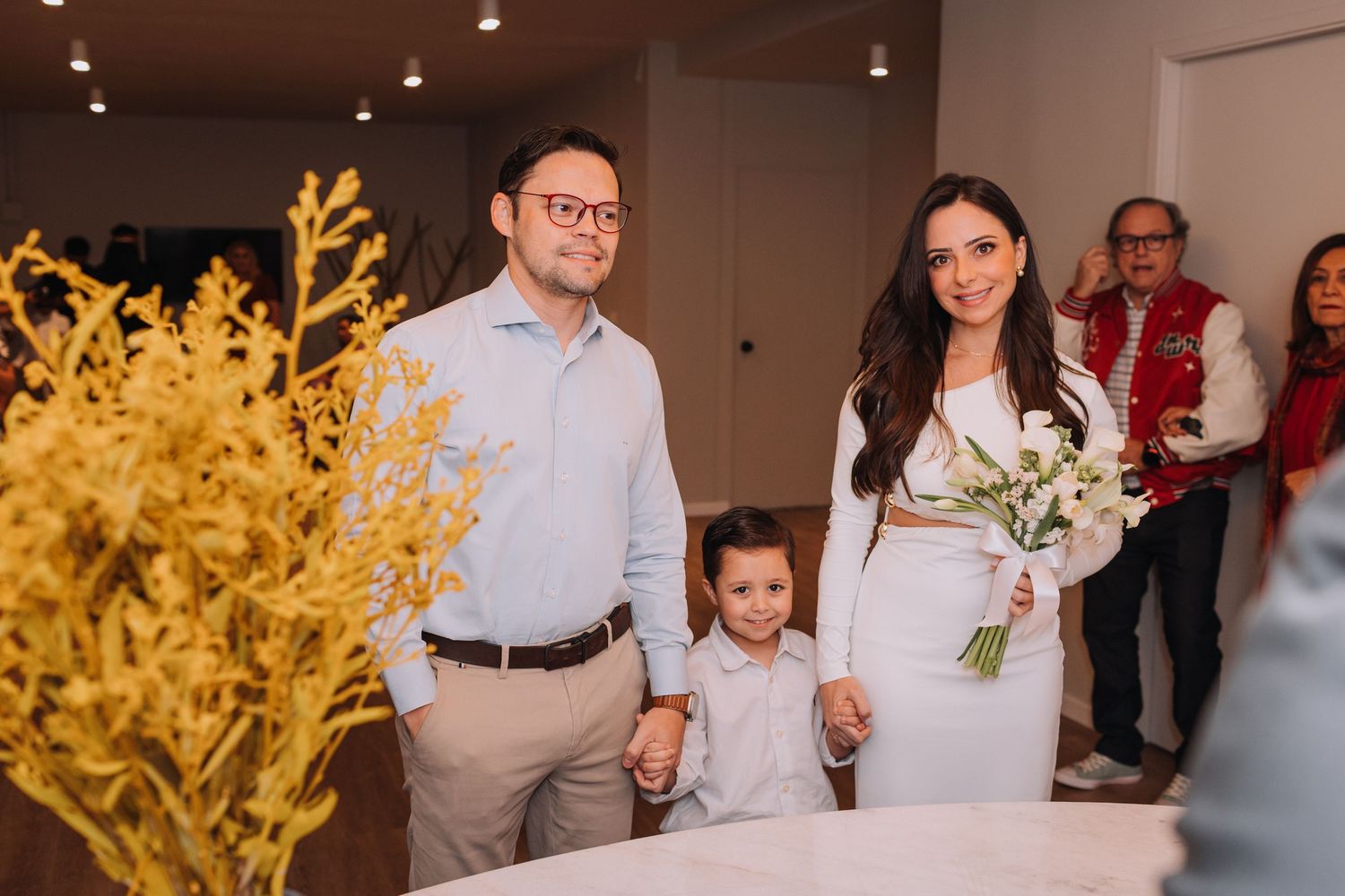 People celebrating at an indoor event with yellow floral decorations and warm lighting.