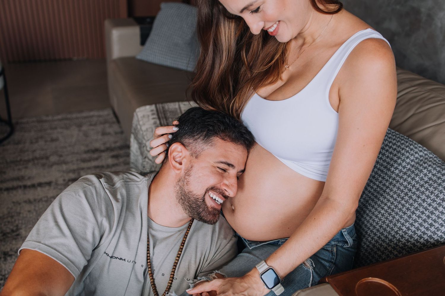 Intimate maternity moment captured on a comfortable grey sofa.