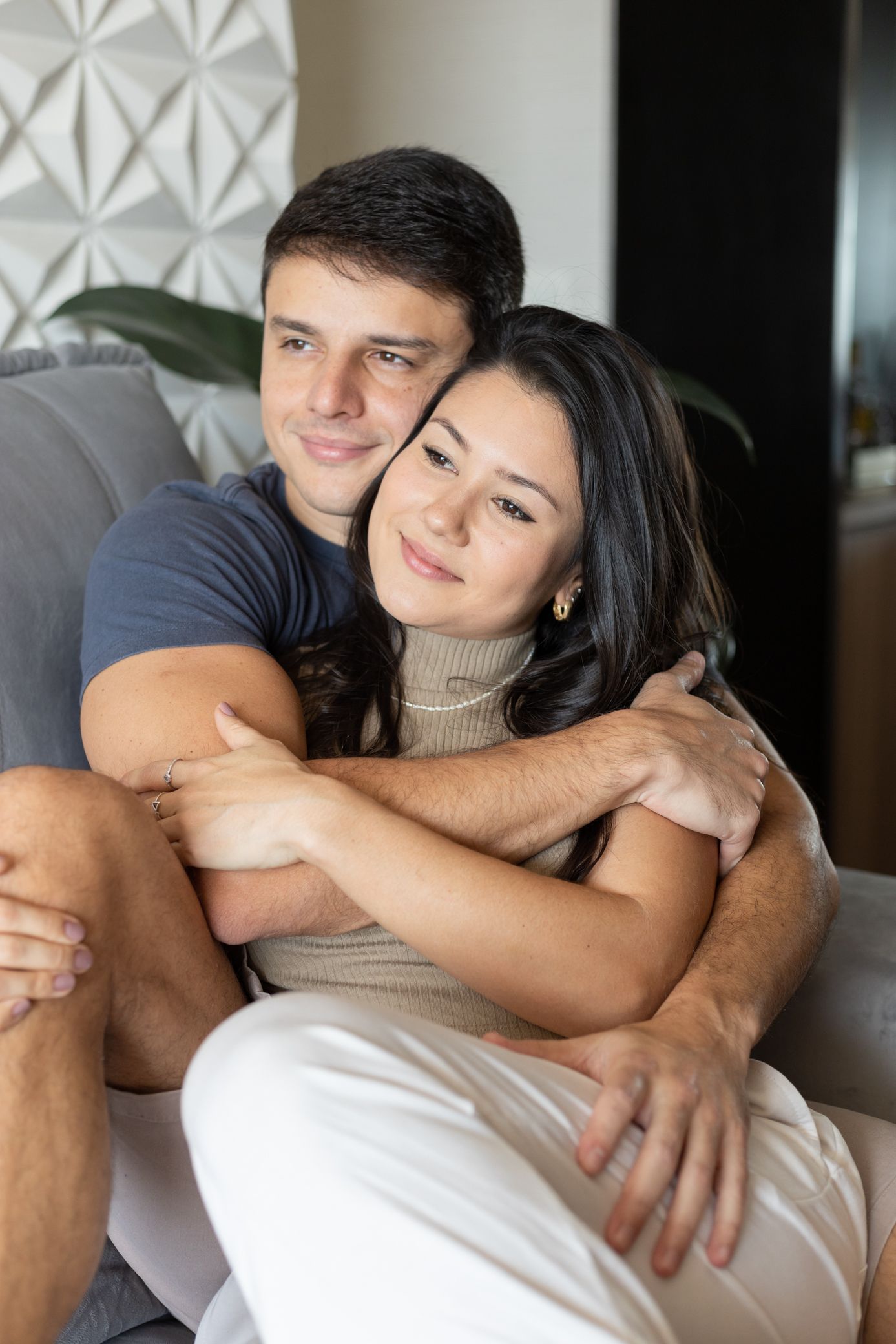 A young couple sitting on a couch, smiling and embracing each other in a cozy living room.