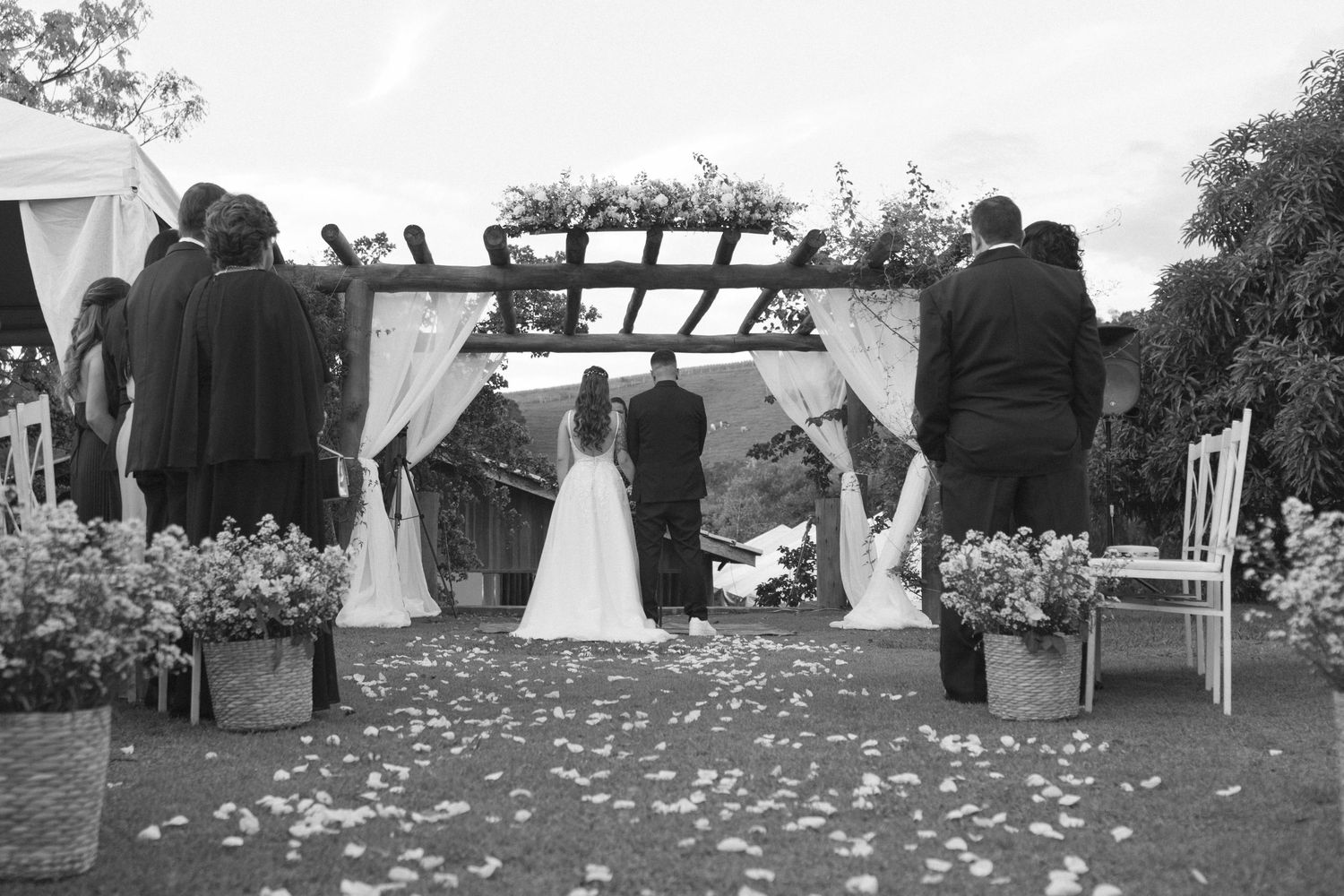 A romantic outdoor wedding ceremony with white tents and rose petals scattered along the pathway.