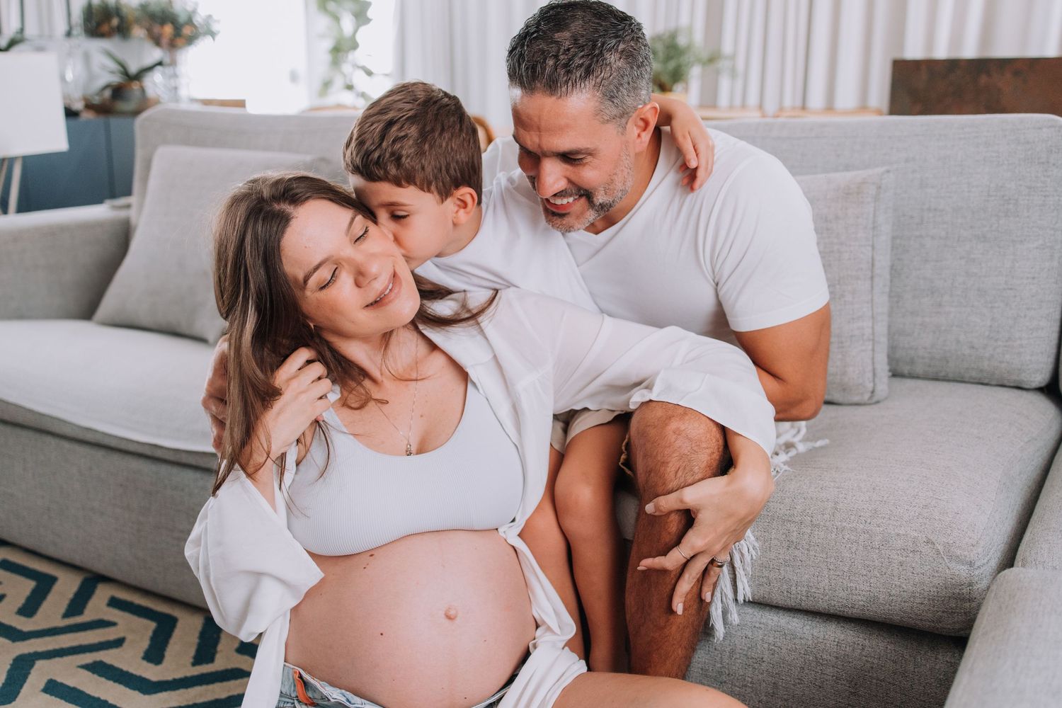 Family maternity session captured in bright modern living room with blue artwork.