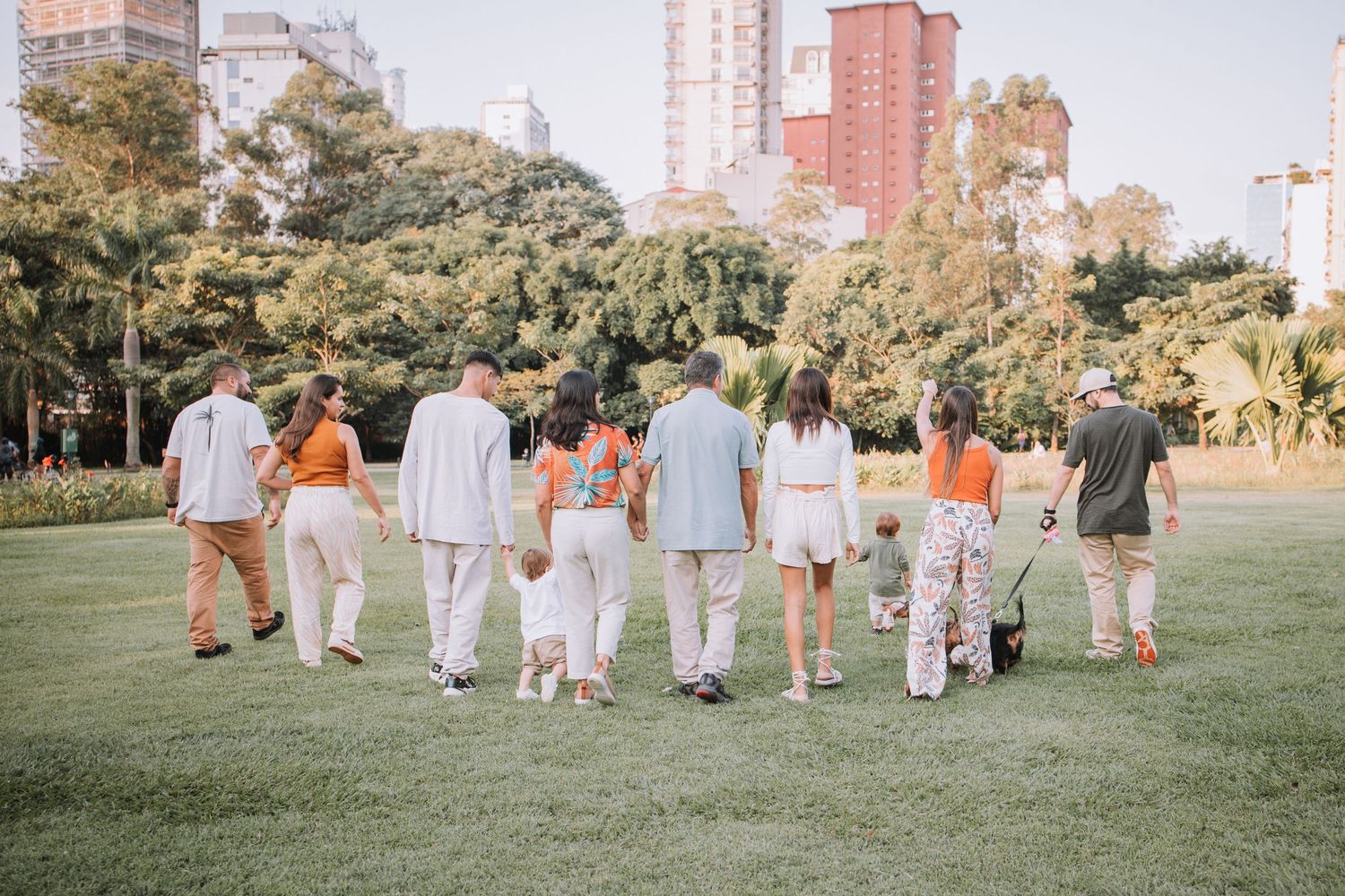 Family members walking in line across grassy field with city buildings in background.