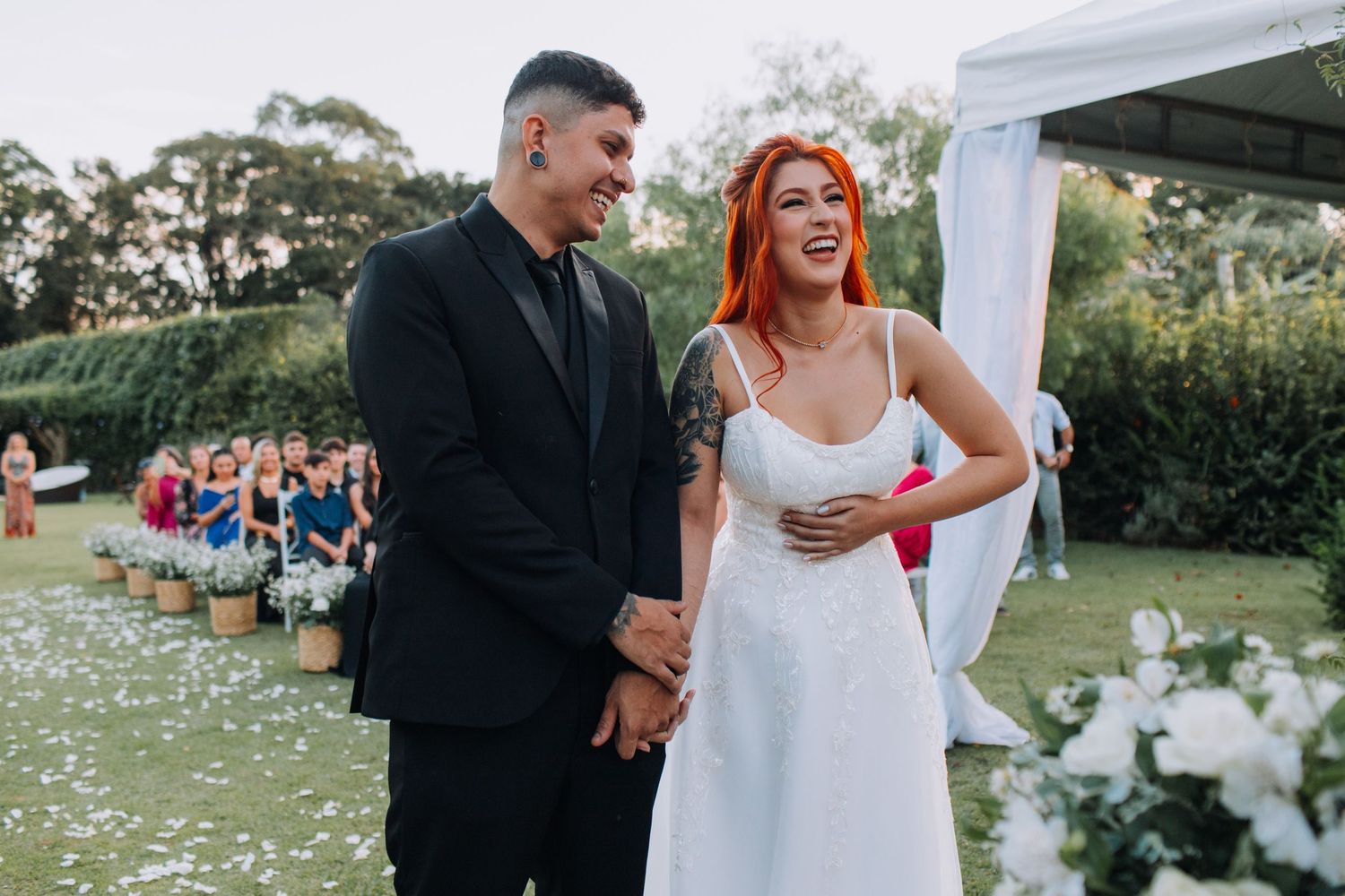 A couple shares a joyful moment during their outdoor garden wedding ceremony surrounded by flowers and guests.