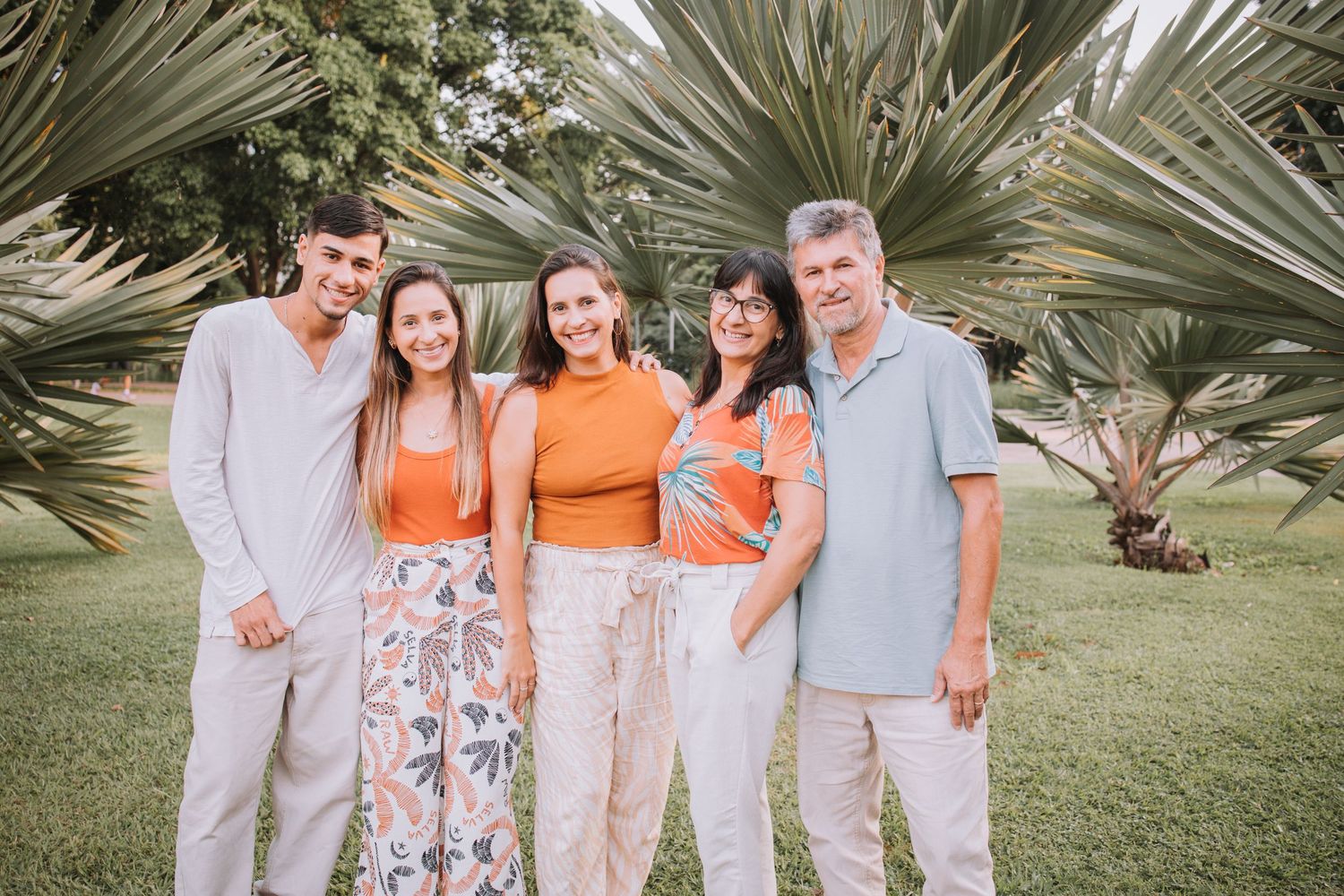 Family portrait with matching outfits in white and orange against tropical landscape.