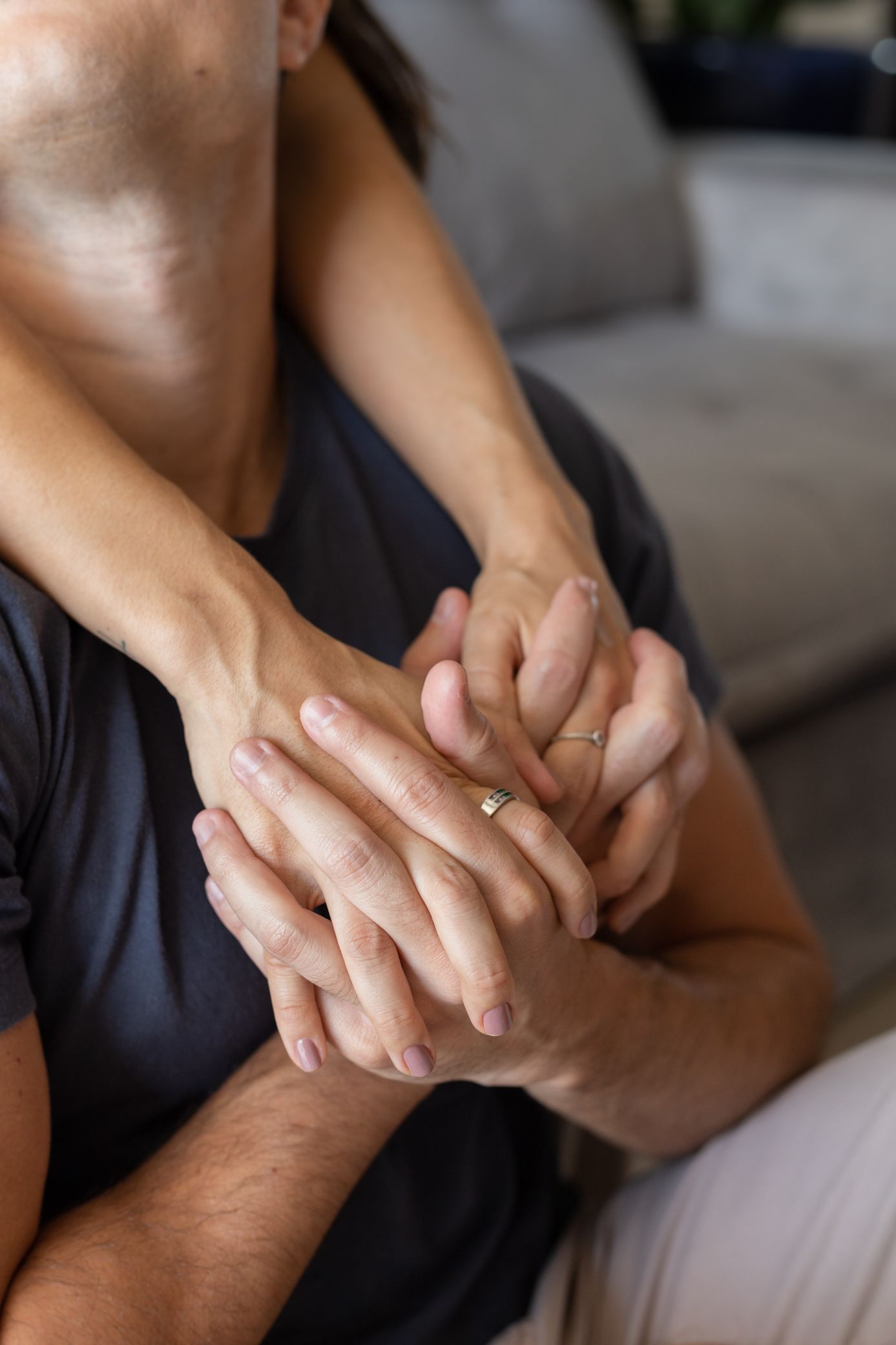 Close-up of a couple holding hands tenderly on a couch, one wearing a gold ring, symbolizing love and connection.