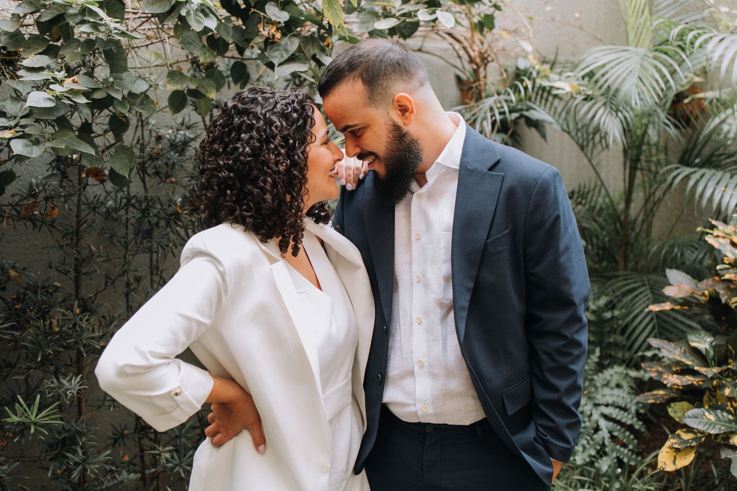 A romantic couple shares intimate moments in a lush garden setting with greenery and natural lighting.