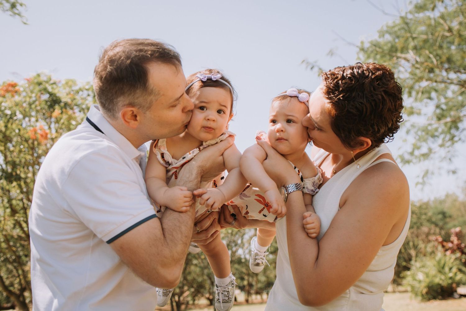 Parents playing with baby outdoors in natural sunlit setting.