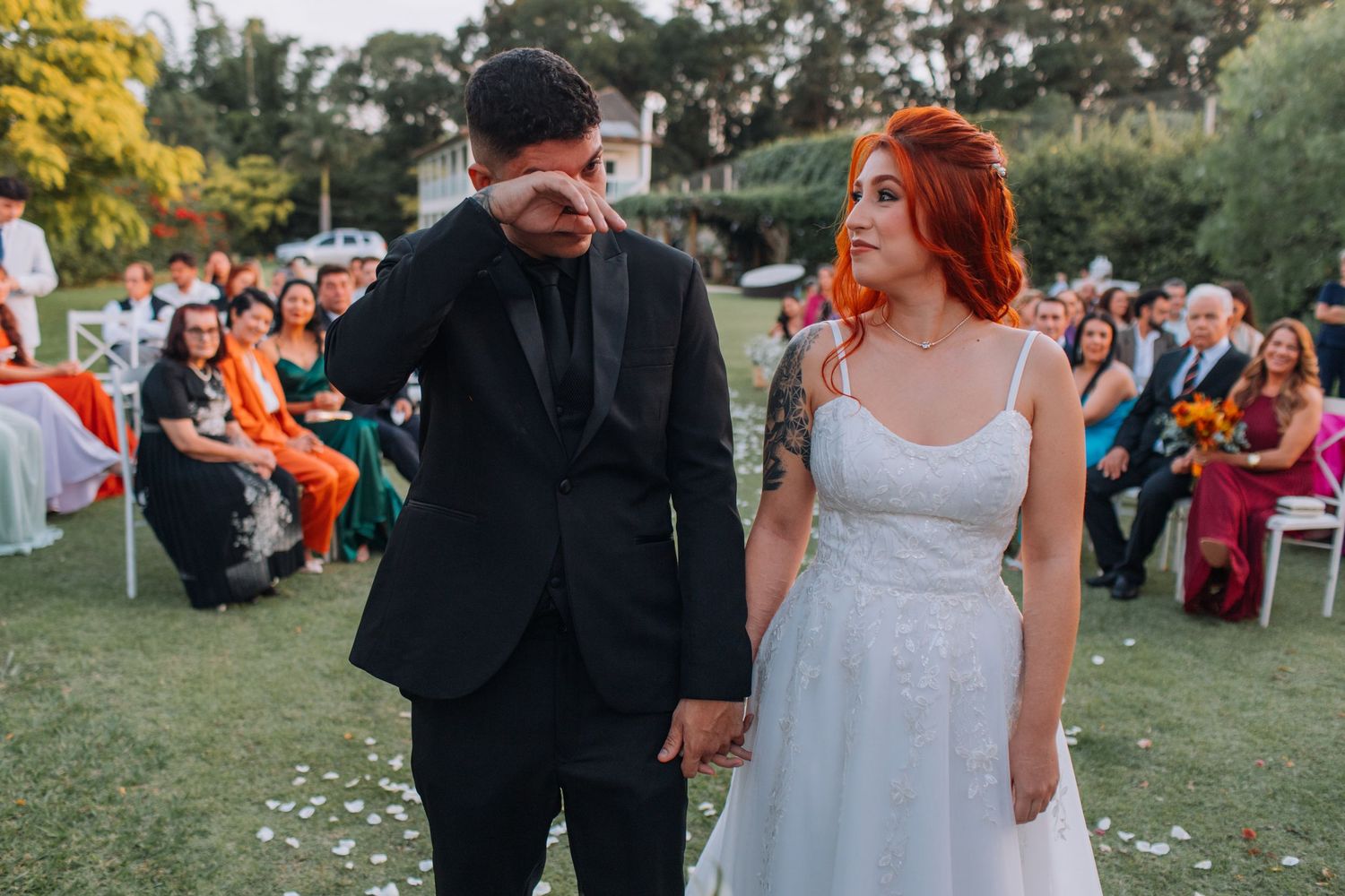 A couple in wedding attire walks together on a grassy lawn during an outdoor celebration.