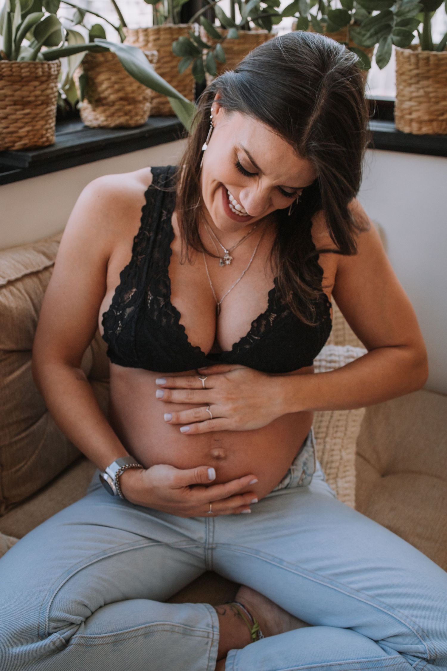 A pregnancy photoshoot on a couch with indoor plants and natural lighting.