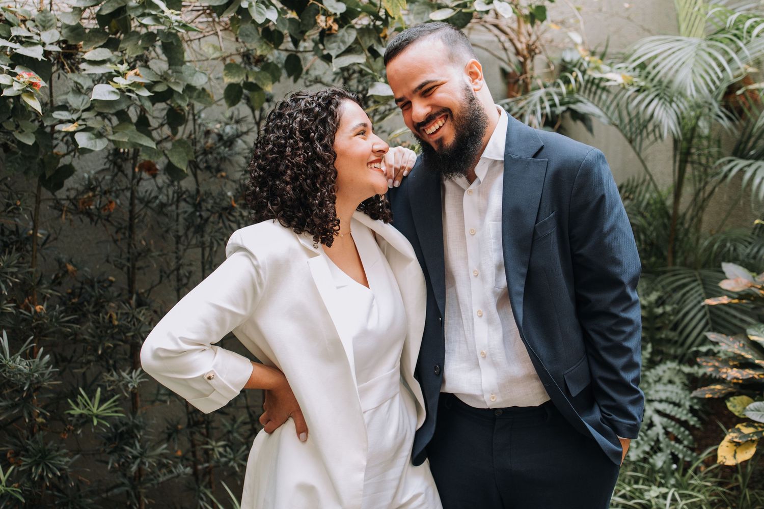 A couple shares joyful moments in a lush garden setting while wearing contrasting white and black formal attire.