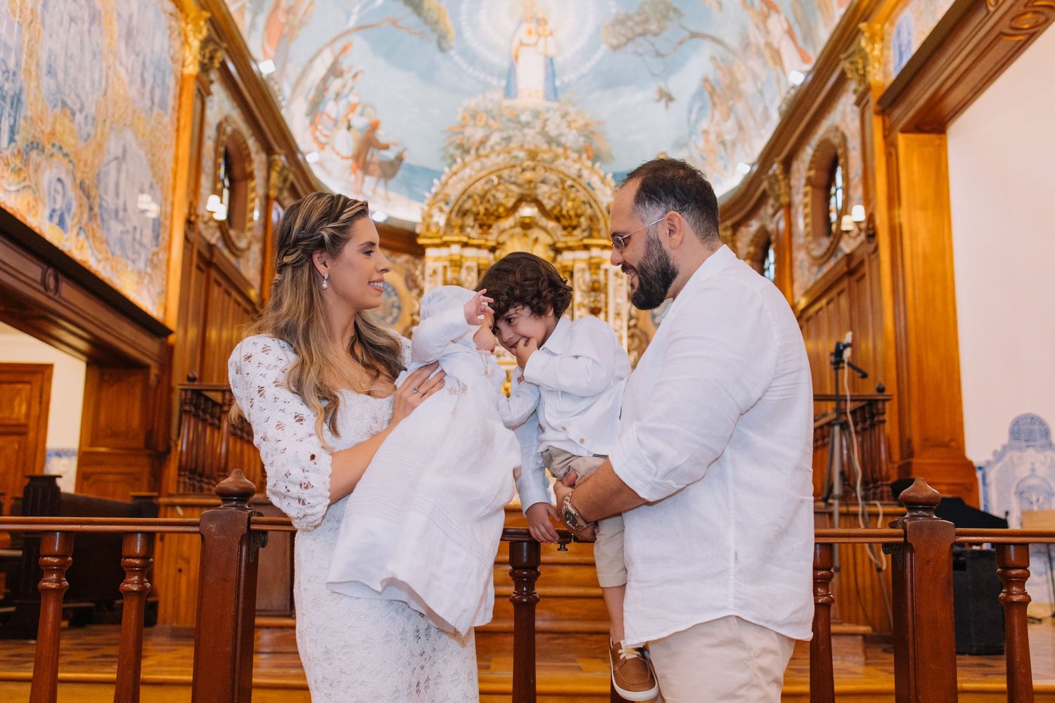 Family in white attire celebrating a baptism ceremony inside an ornate church with beautiful frescoes.
