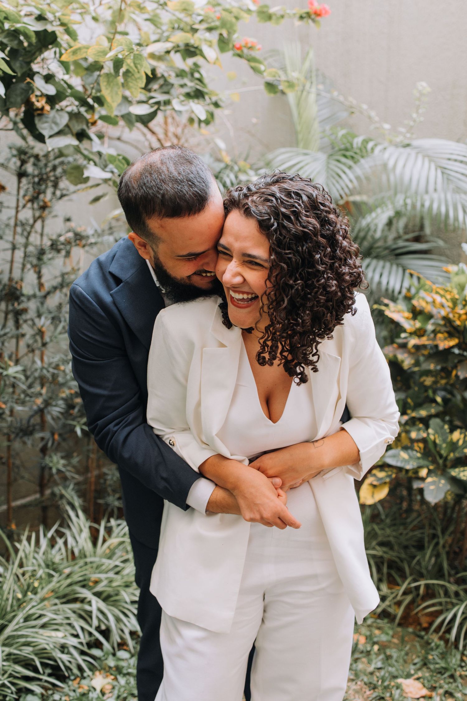 Couple in coordinated white outfits sharing joyful moments in a garden.