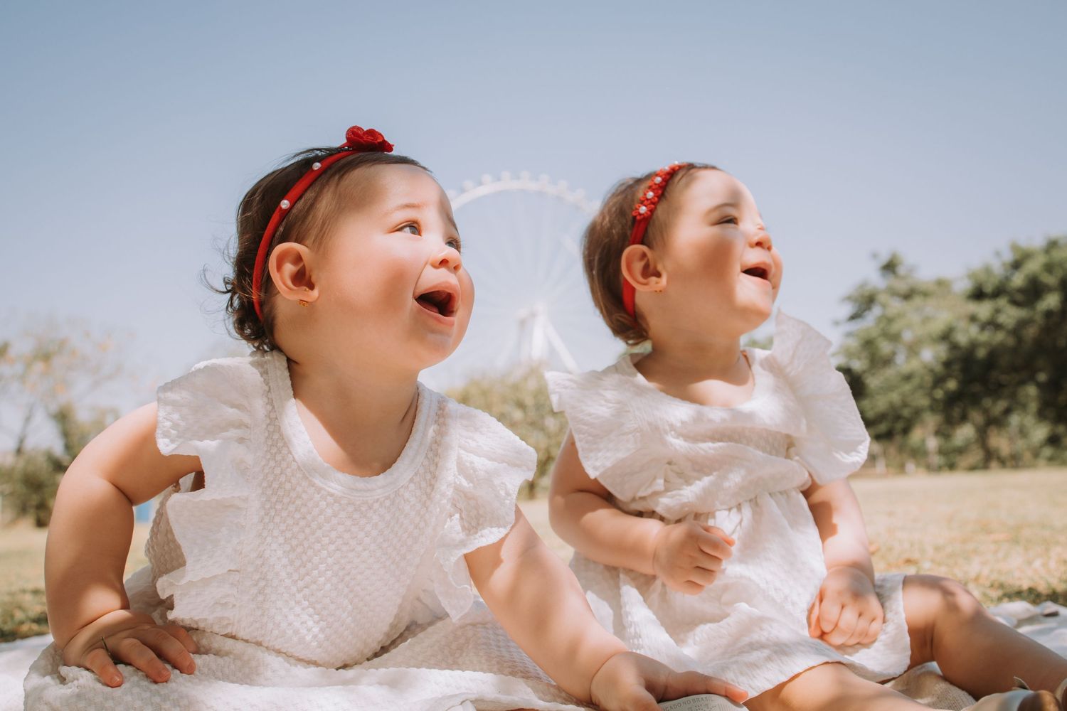 Two children laughing and playing together on a white blanket outdoors.