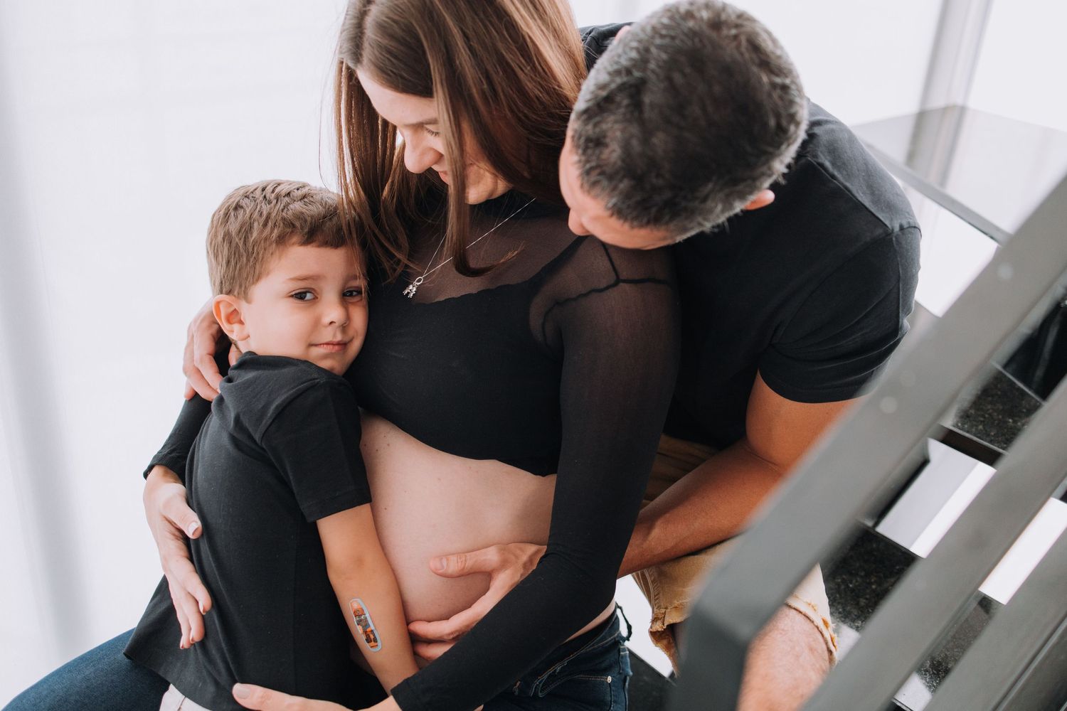 Family gathers on stairs for intimate maternity photo with young child.