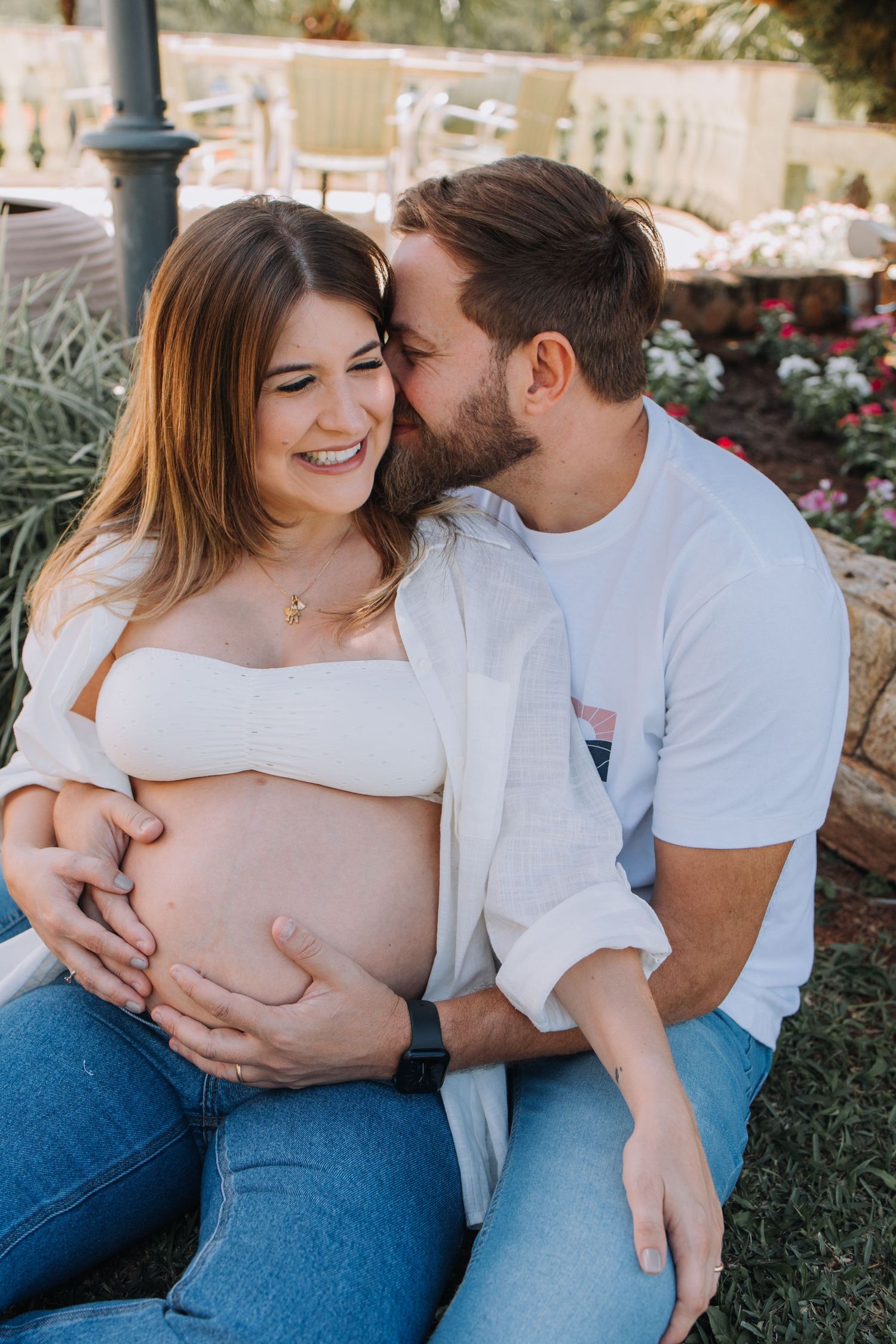 Couple shares intimate outdoor maternity moment in garden setting.