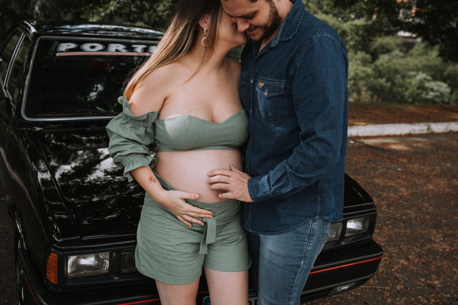 Couple poses with vintage black car during outdoor maternity photography session.