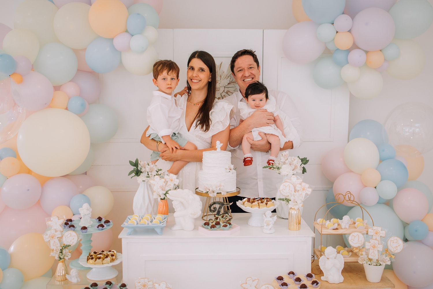 Pastel balloon arch decorates a white room with soft lighting for a celebration.