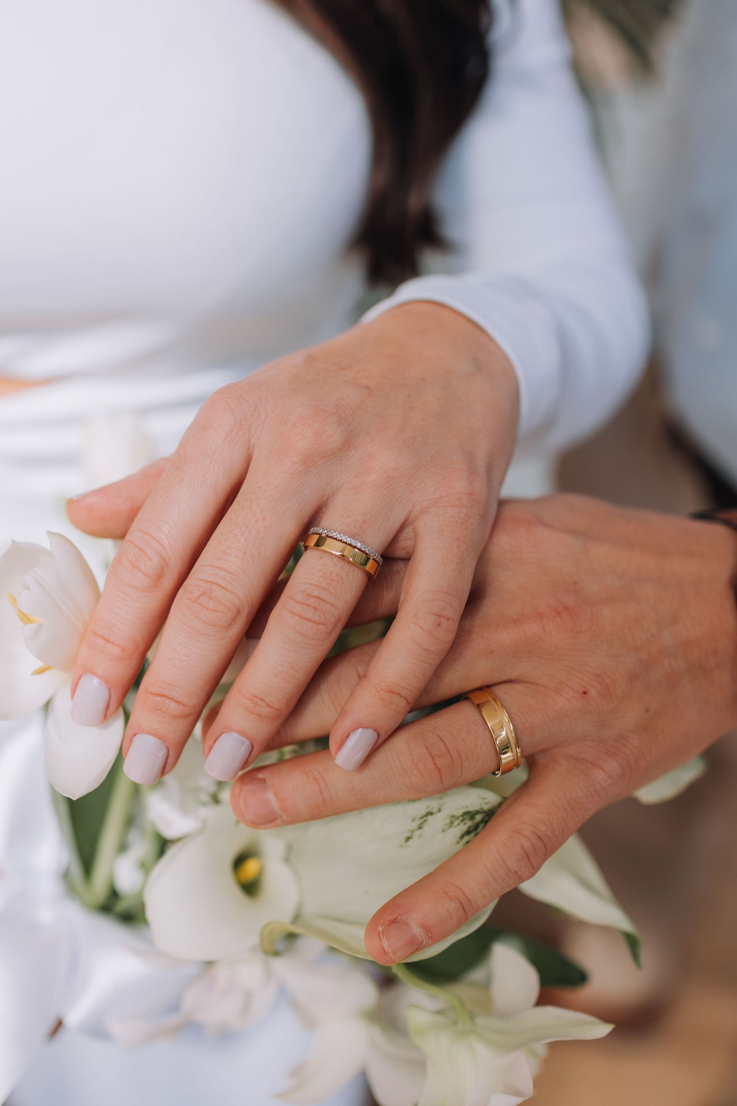 Close-up view of hands wearing wedding rings while arranging white flowers and delicate floral decorations.