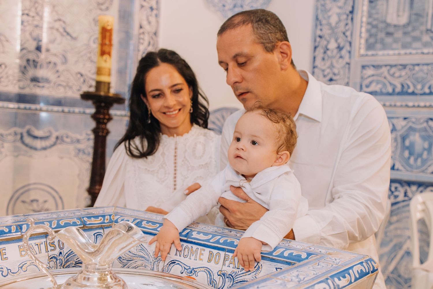 Family celebrating a baby baptism in a blue and white decorated church, parents holding infant at the baptismal font.