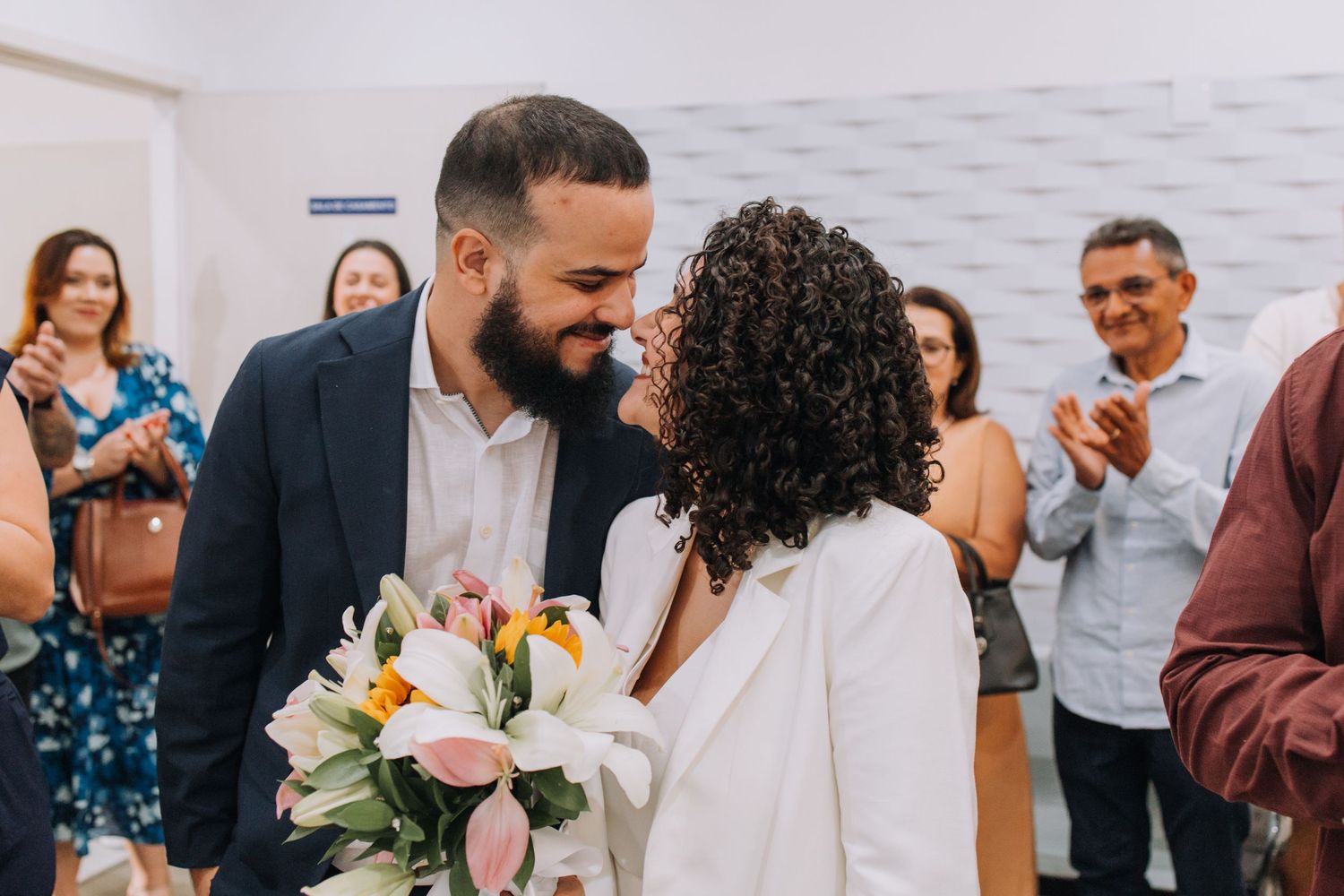 A happy couple shares a joyful moment at their wedding celebration while guests applaud in the background.