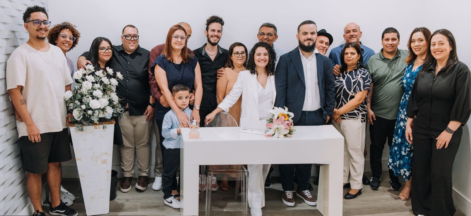 Large group photo of wedding guests standing together against a white wall at a celebration.