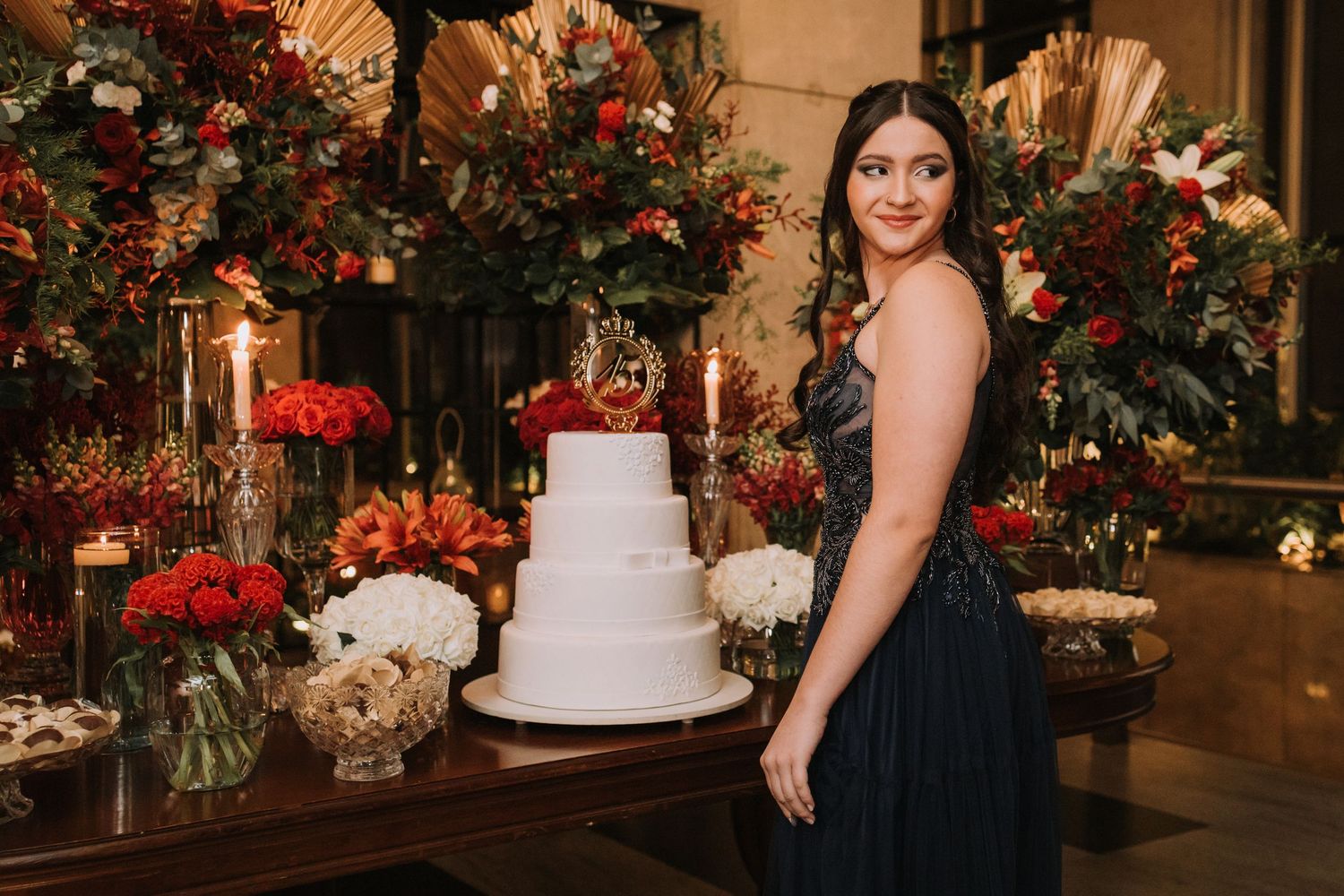 Wedding reception venue decorated with elegant floral arrangements and a white tiered cake in warm ambient lighting.