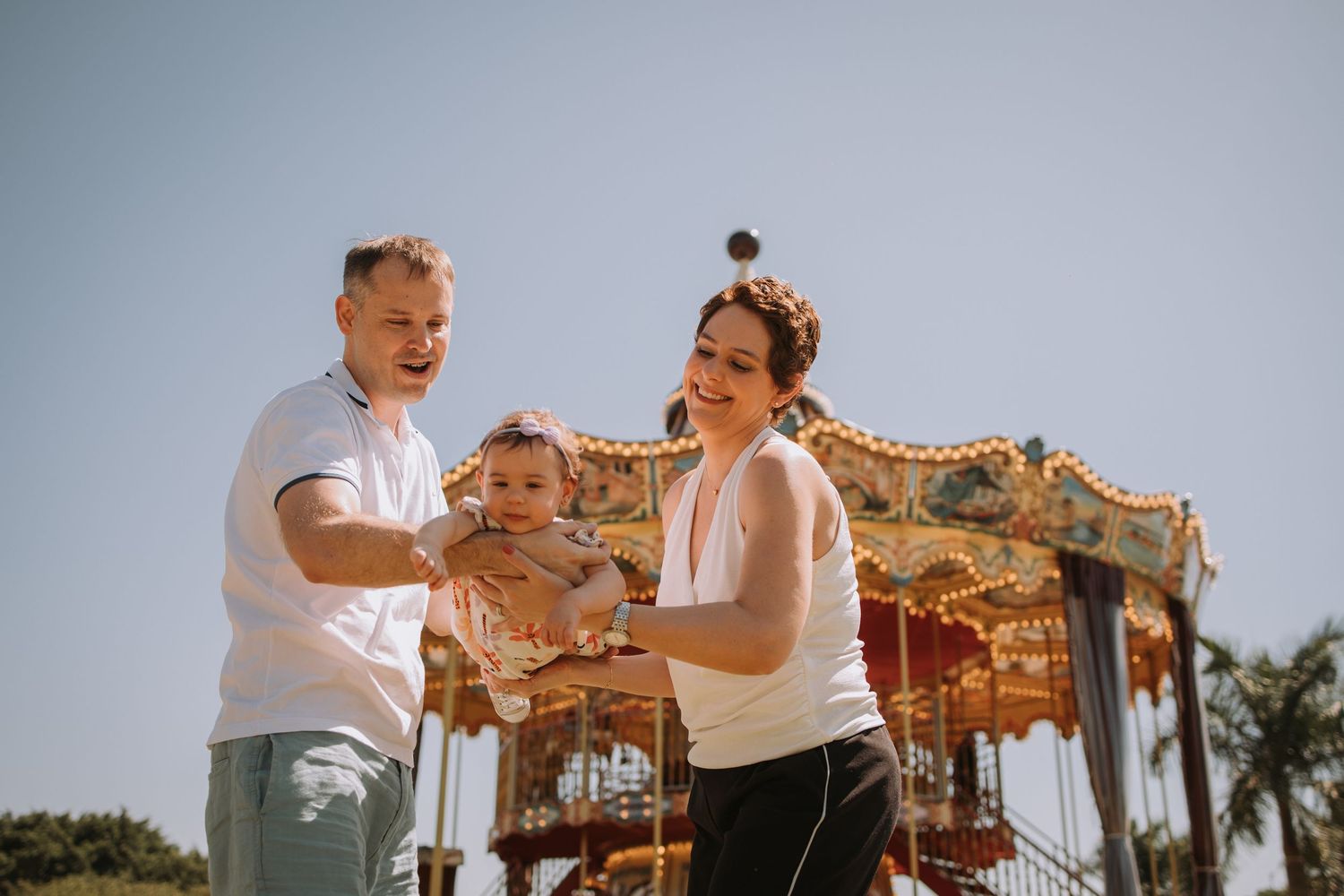Family posing together near a decorative carousel on a bright sunny day.