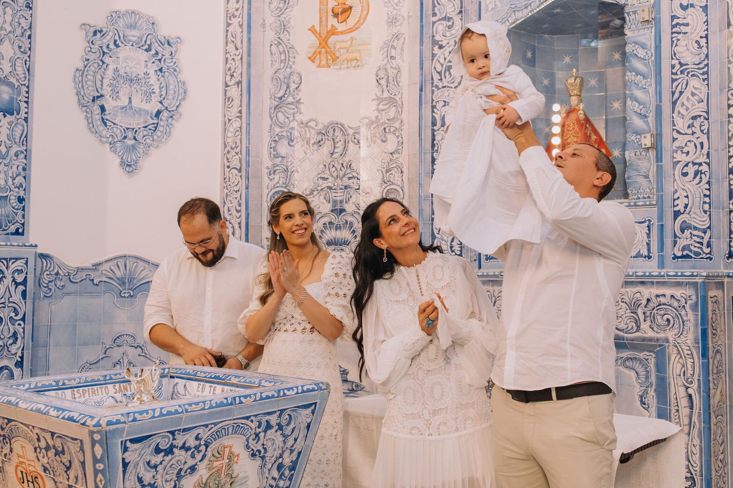 People in white attire seated together against a backdrop of decorative blue and white tiles.