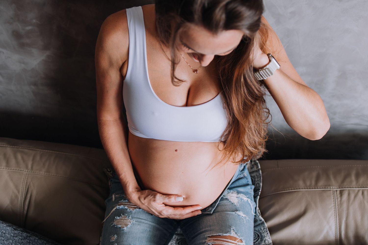 Casual maternity photo session on a grey couch with natural lighting.