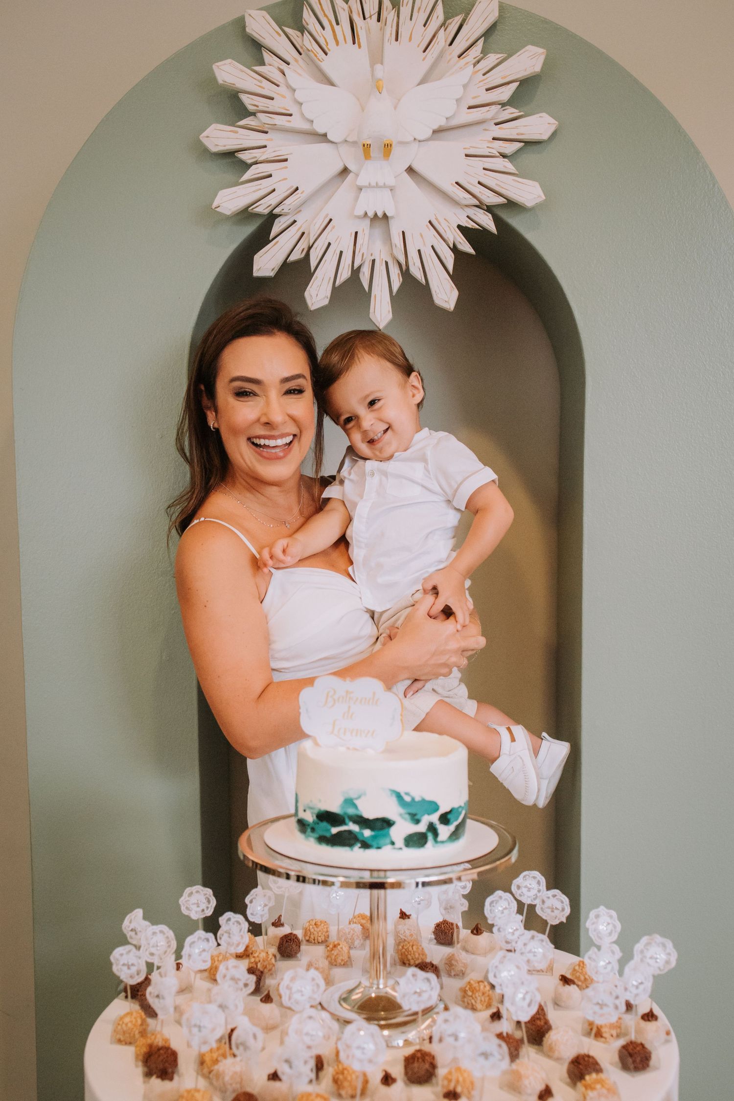 A dessert table with white cake and cupcakes decorated with a large white starburst decoration against a sage green wall.