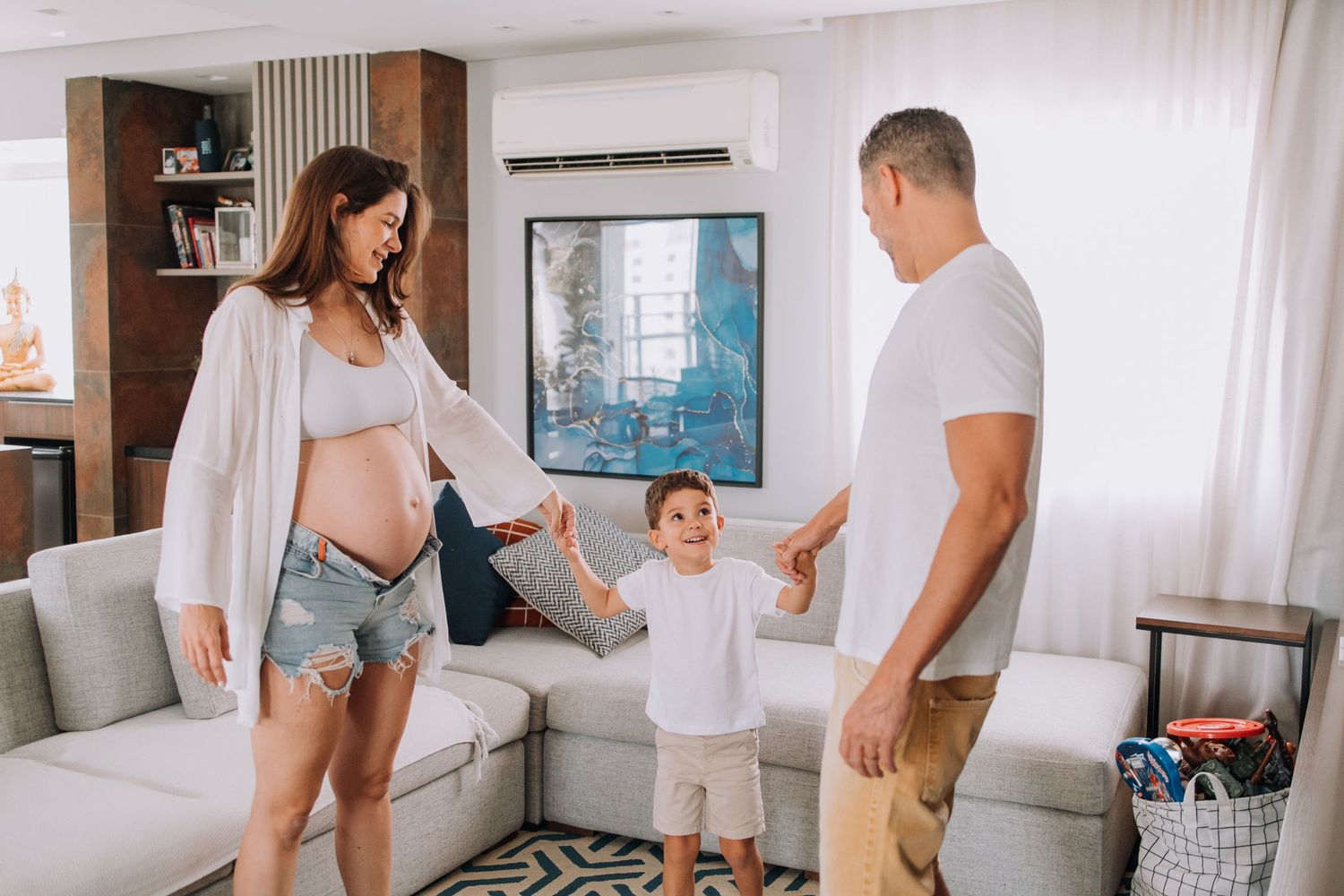 Family plays together in modern living room with toddler jumping between parents.